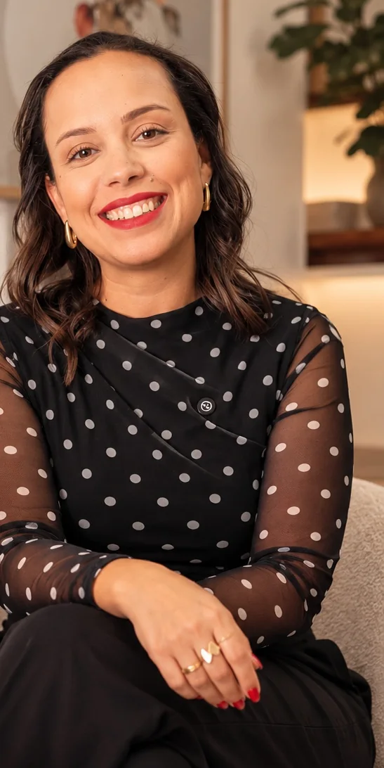 Idma Socha sentada na poltrona do consultório, sorrindo, de blusa de poá